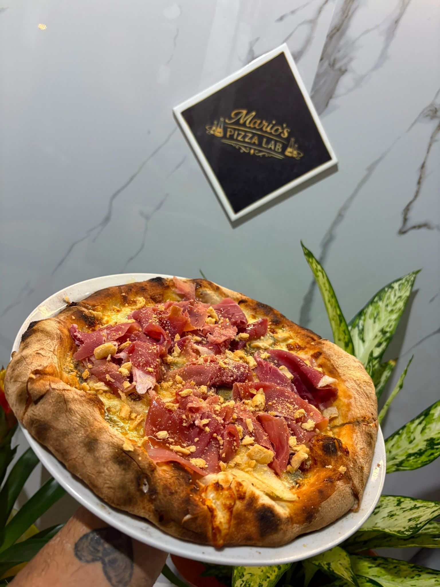 Pizza cotta nel forno a legna su un piatto bianco accanto a un'insegna con il logo del locale in un ristorante moderno.