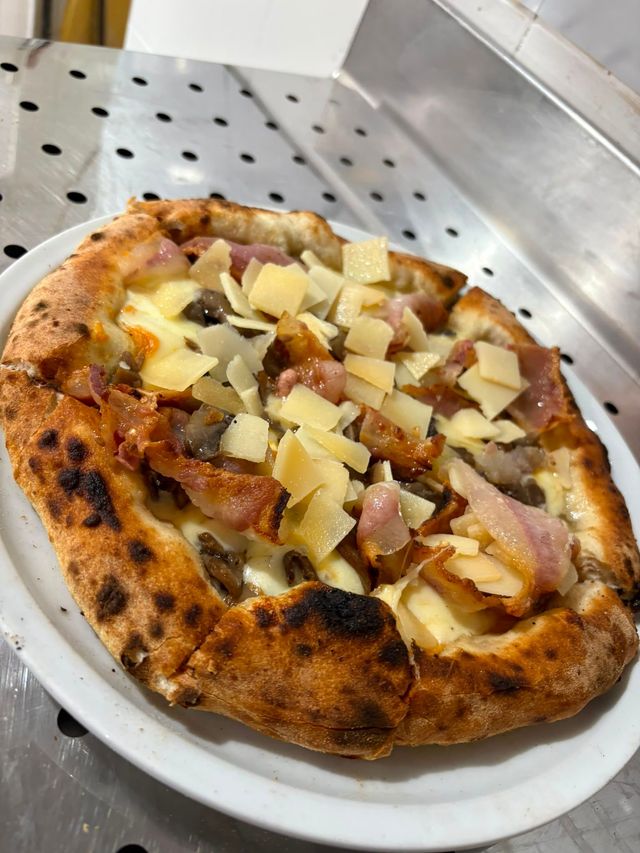 Una fetta di pizza con patate a cubetti e pancetta su un piatto bianco appoggiato su un bancone in acciaio inox.