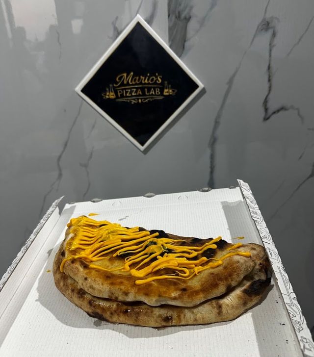Pizza al formaggio su una scatola bianca davanti all'insegna di Marcio's Pizza Cafe su una parete di marmo.