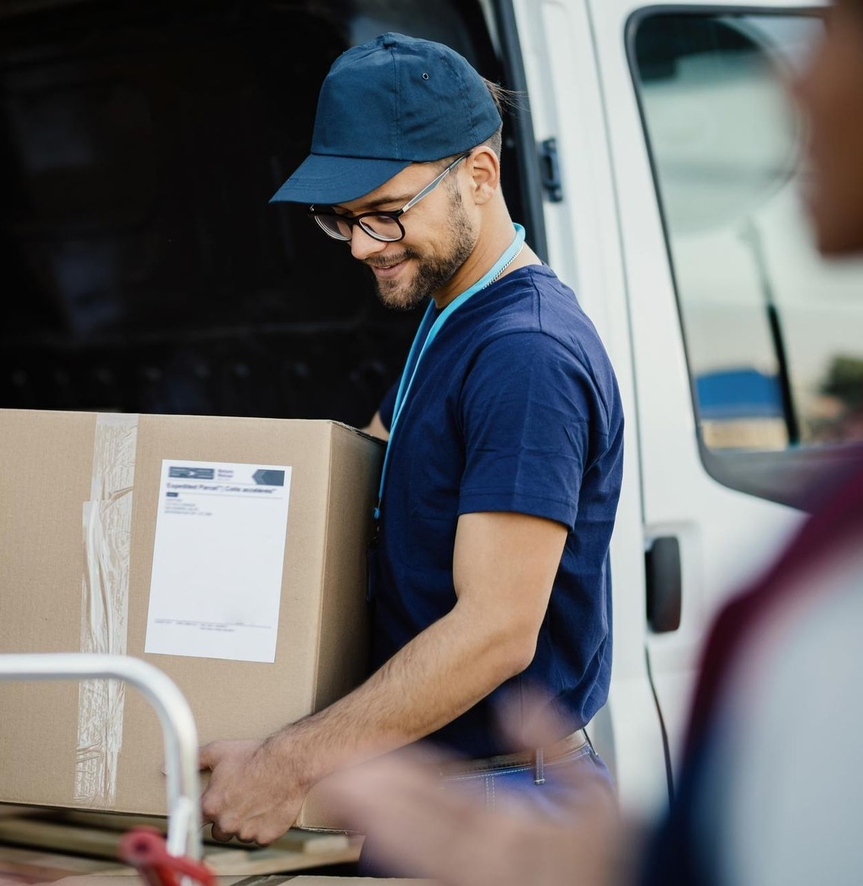 Delivery person in blue uniform and cap, unloading a cardboard box from a white van.