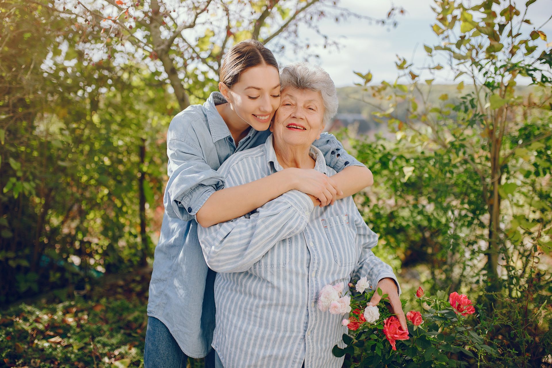 Young person hugging an older person outdoors by a rose bush. They're smiling.