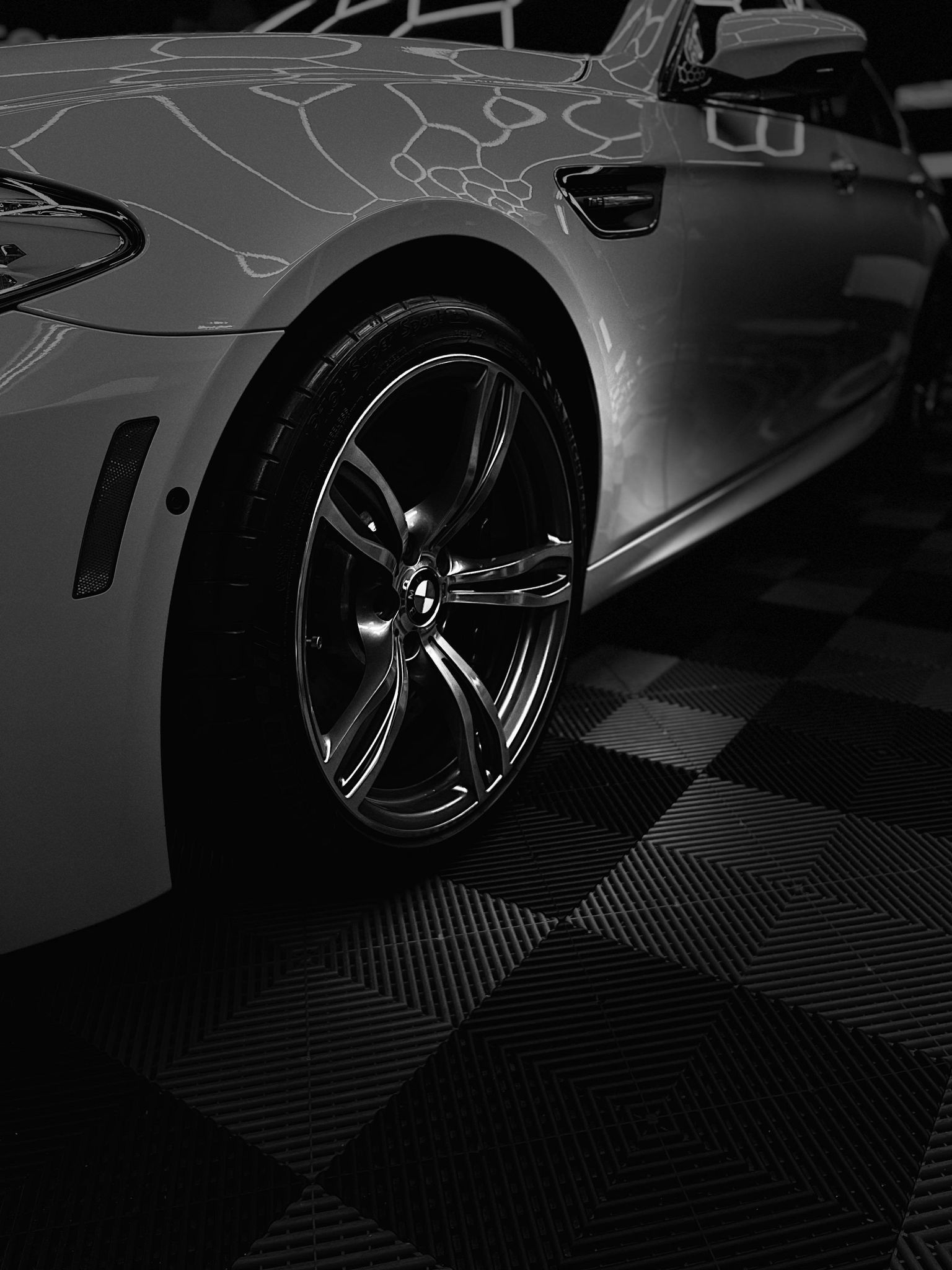 Glossy silver sports car side view with black wheels on patterned showroom flooring