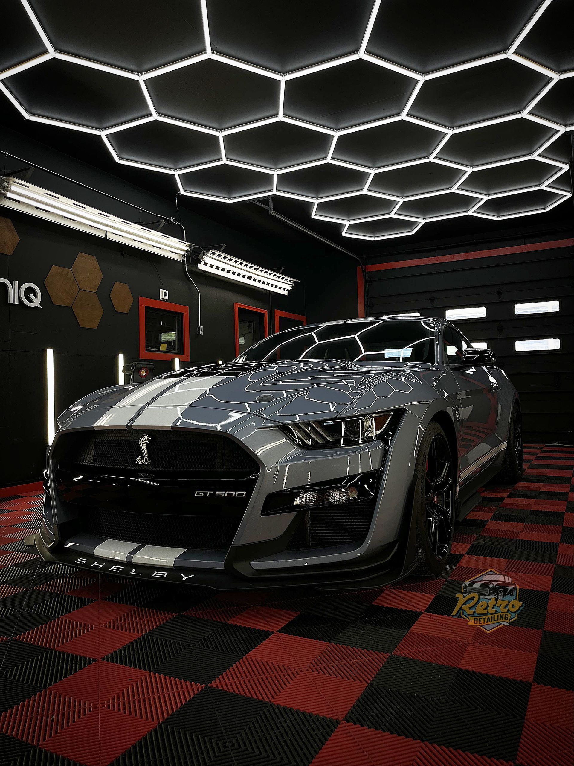Silver sports car in a neon-lit showroom with hexagonal ceiling lights and red-and-black checkered floor