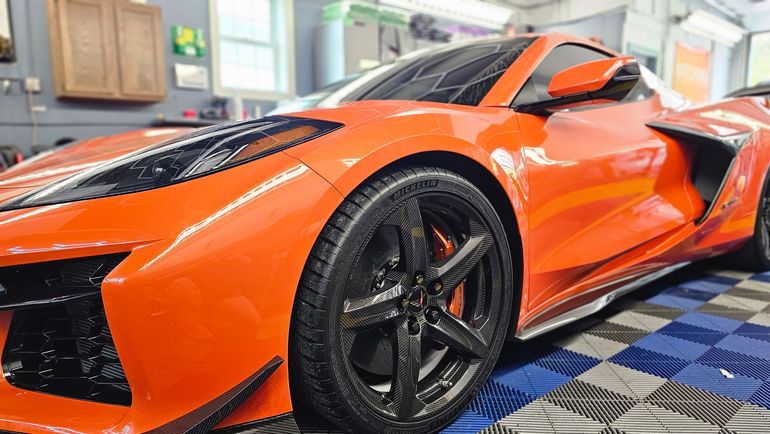 Orange sports car parked indoors on a tiled floor, viewed from the front side.