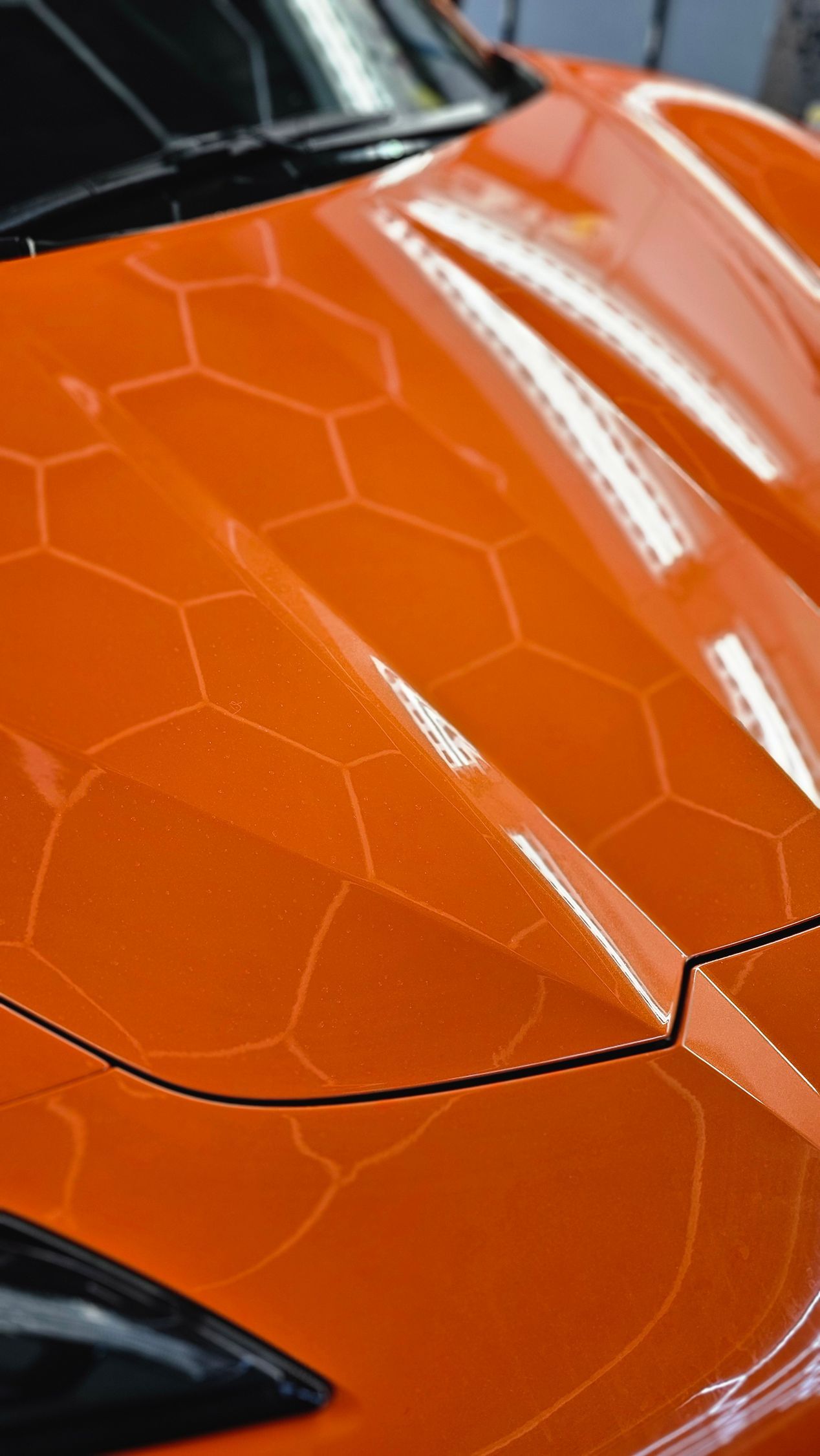 Close-up of an orange sports car hood with a hexagonal textured pattern