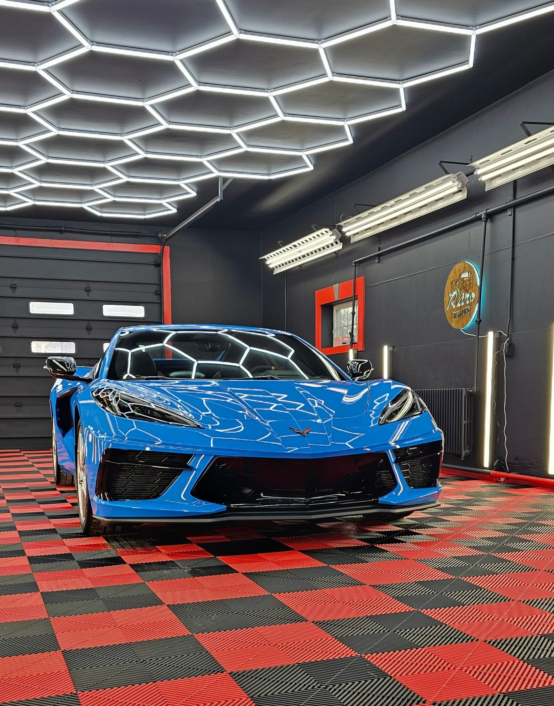 Blue sports car in a black garage with hexagon ceiling lights and red checkerboard floor