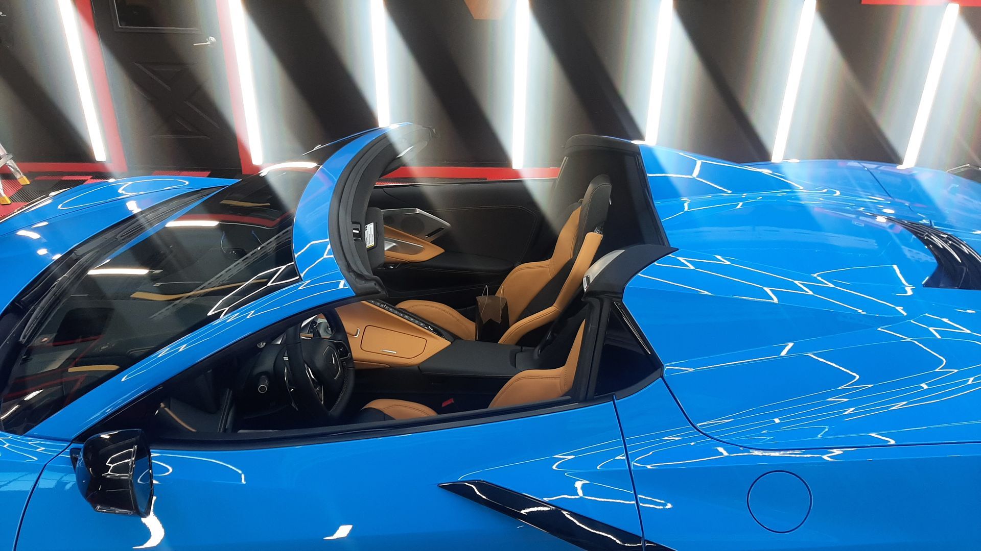Blue sports car cockpit with tan seats and a visible steering wheel, under bright showroom lights