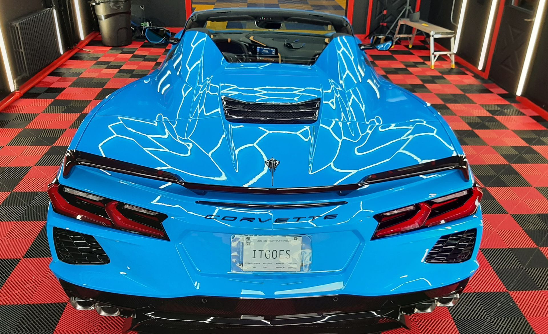 Bright blue sports car rear view on a red-and-black checkered floor in a garage or showroom.