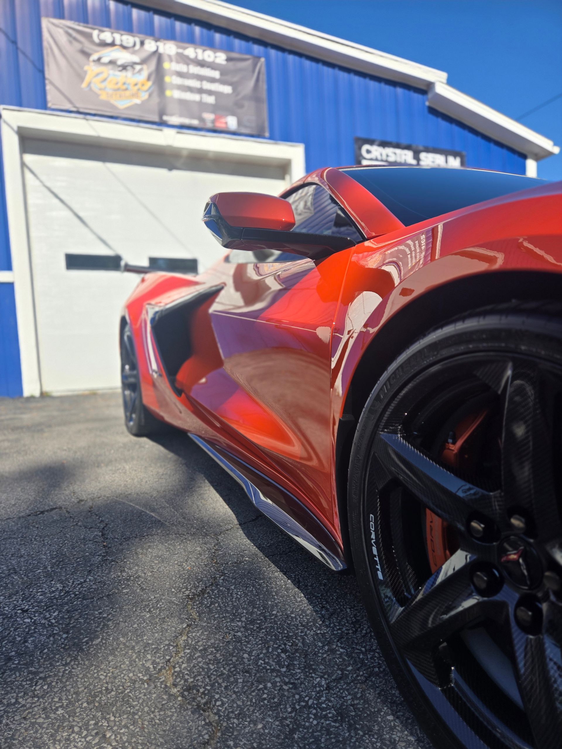 Red sports car parked outside a blue garage, close-up of front wheel and side