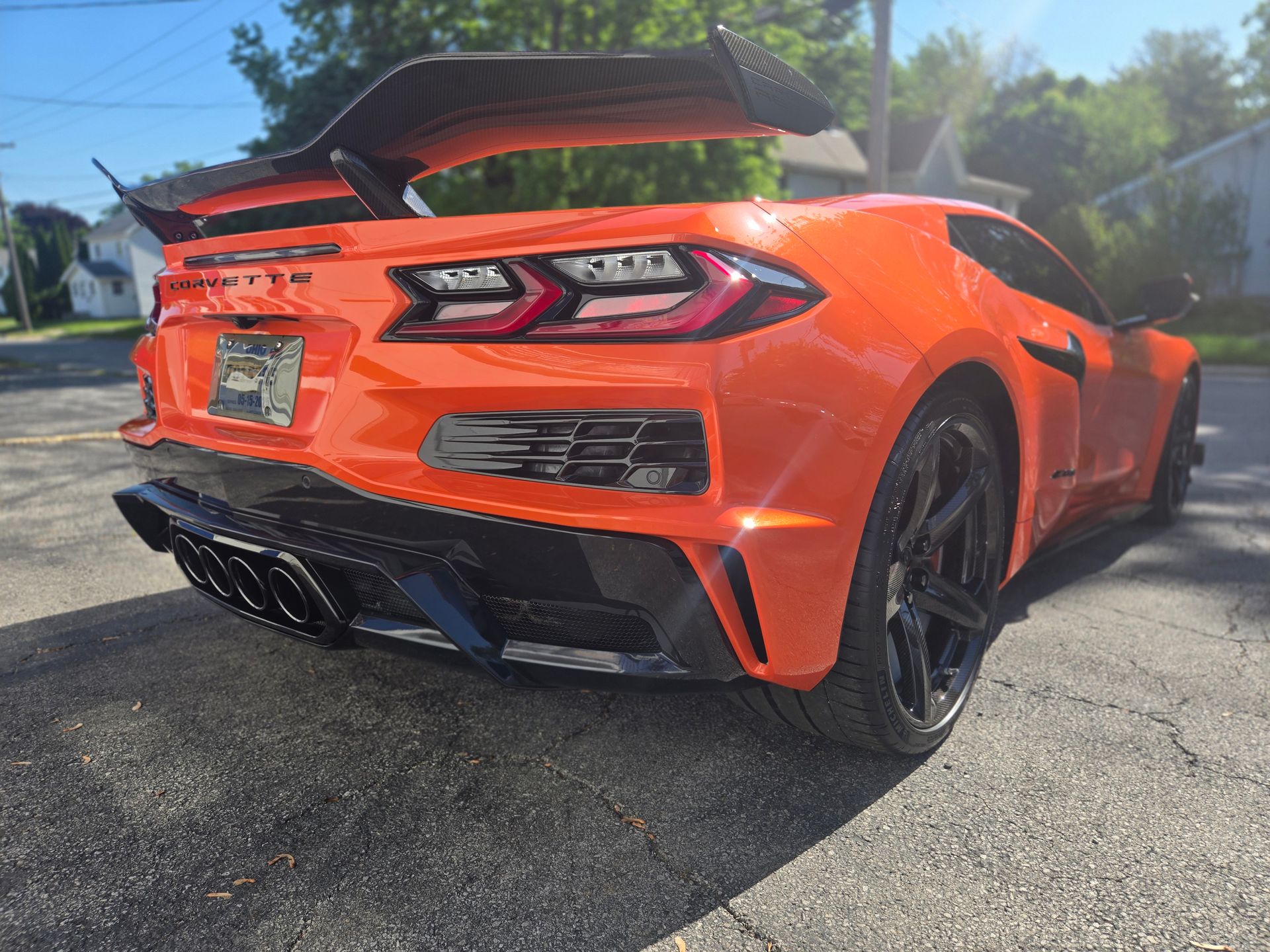 Orange sports car with black accents and rear wing parked on a sunlit driveway
