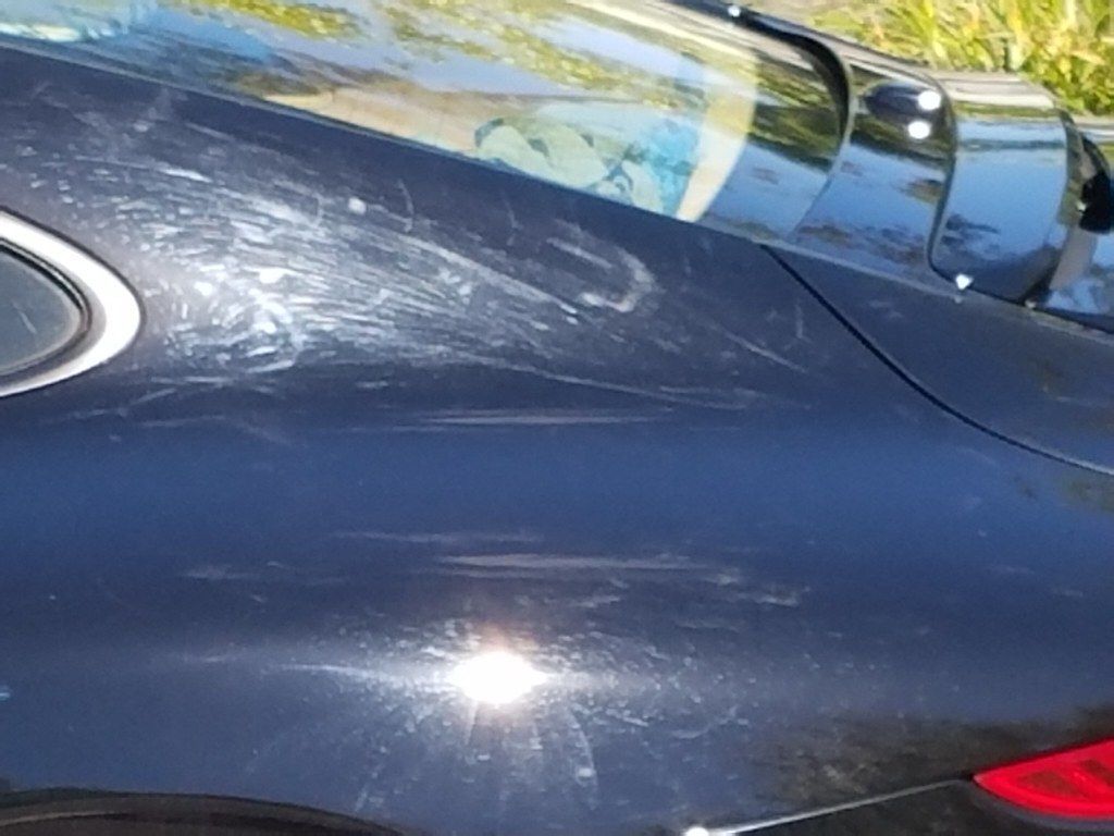 Close-up of a blue car’s side panel with visible scratches and sun glare