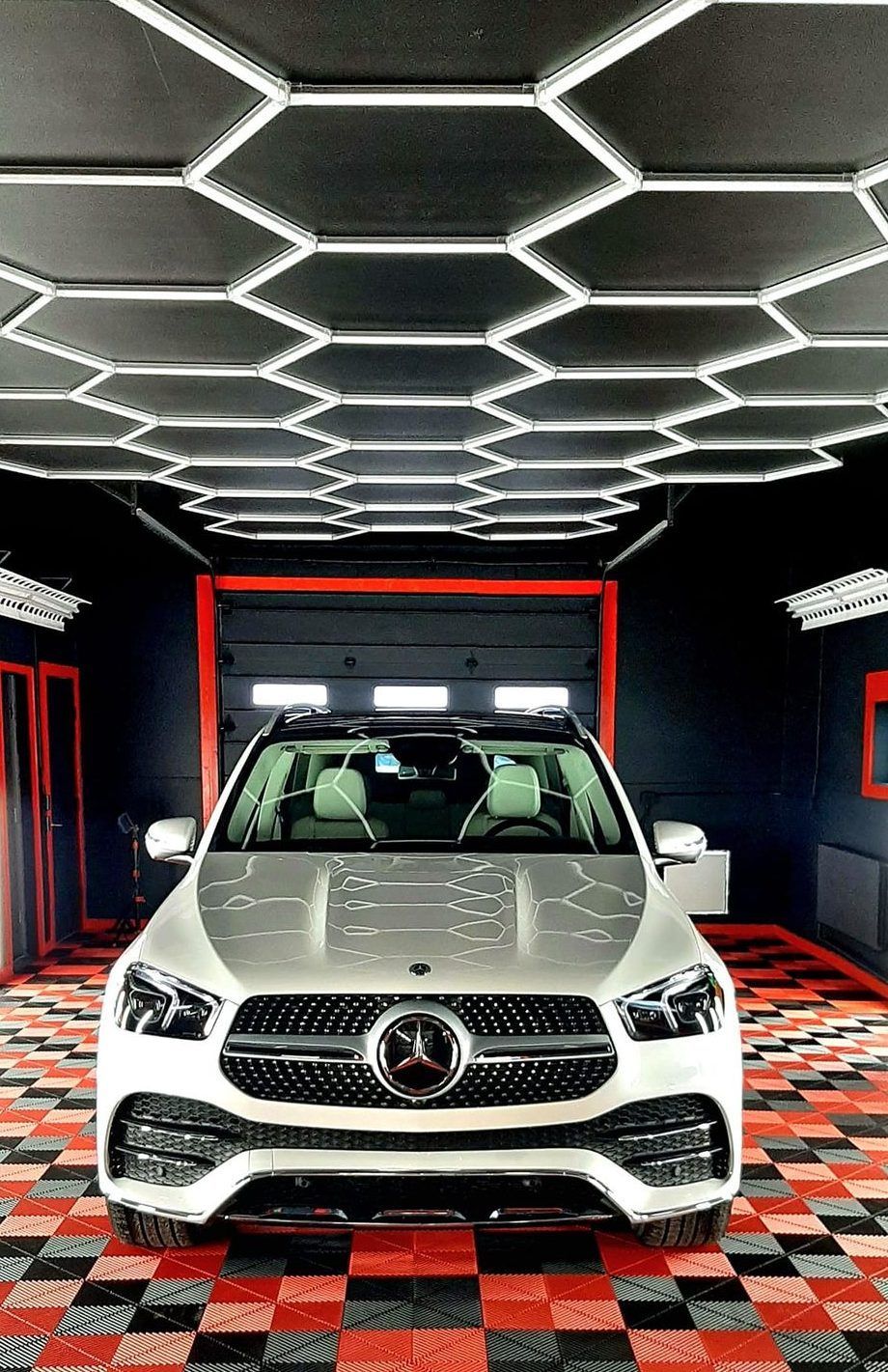 White Mercedes-Benz SUV in a red-and-black showroom with geometric ceiling lights and checkered floor