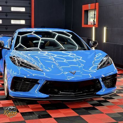 Blue sports car in a dark showroom, front view on a red-and-black checkered floor.