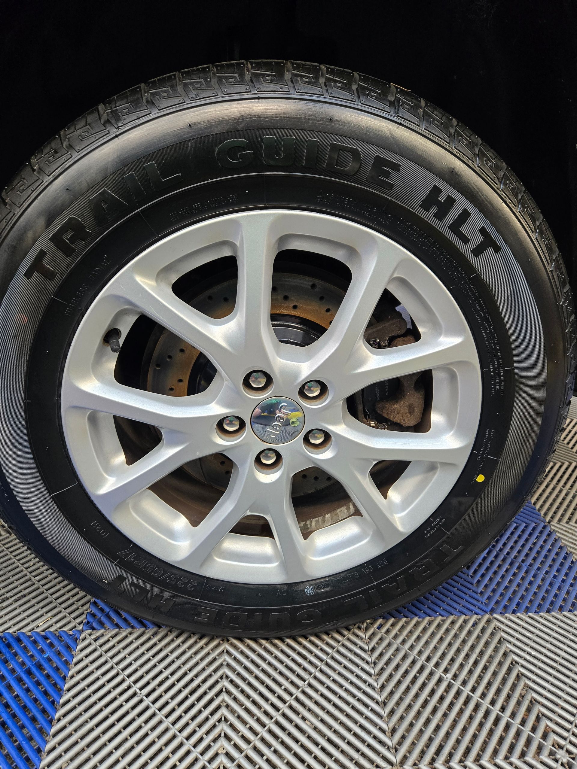 Car wheel with silver alloy rim and black tire on a blue-and-gray checkered floor.