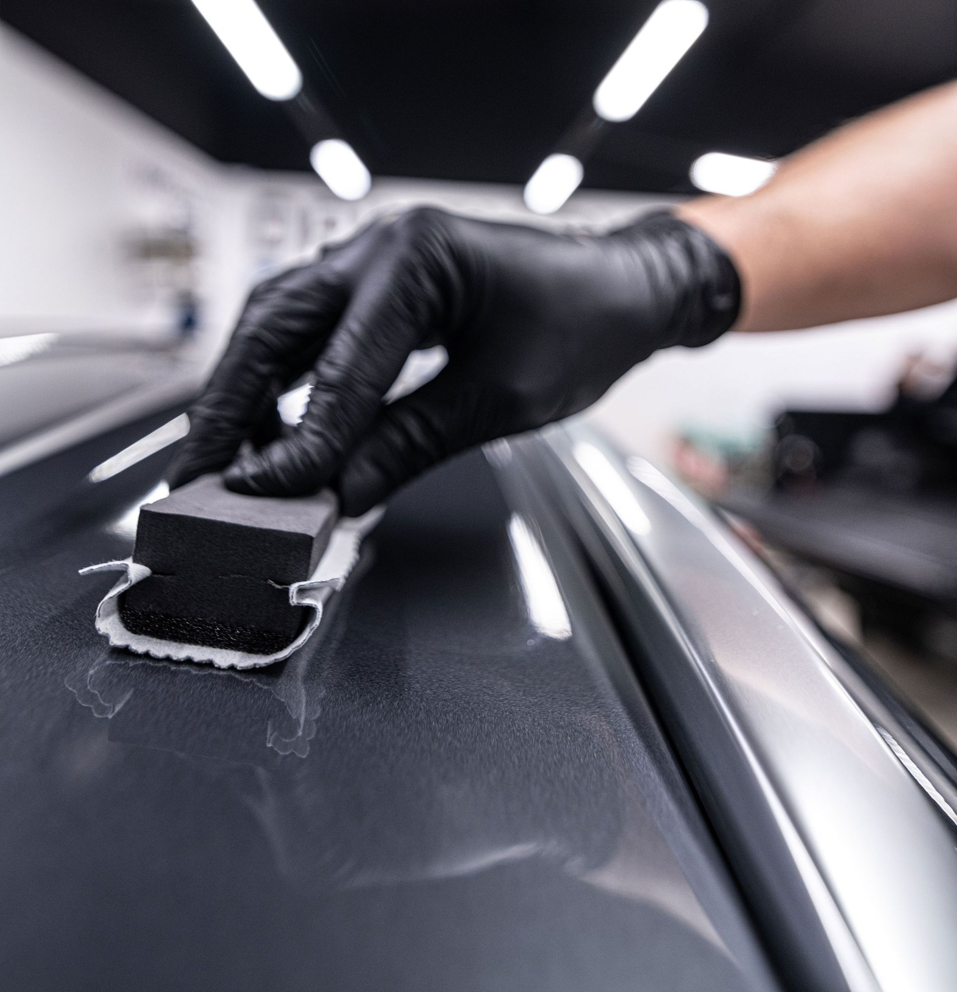 Gloved hand applying a black pad to a glossy car roof in a detailing shop
