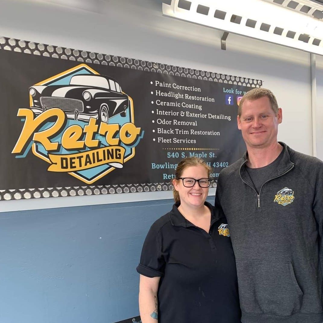 Two people posing in front of a Retro Detailing sign inside a shop