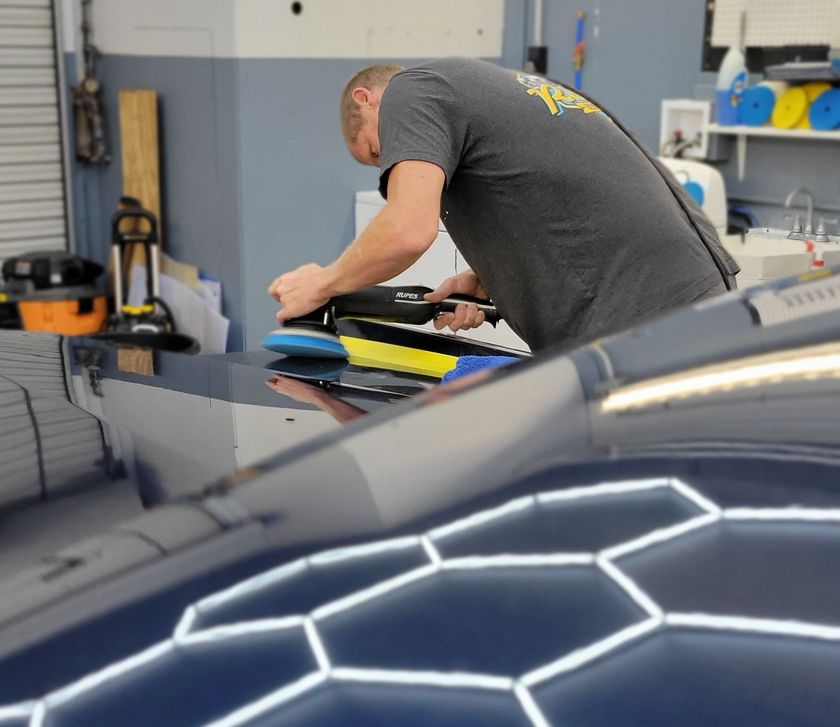 Person polishing a black car hood in a garage, with cleaning cloths and supplies nearby.