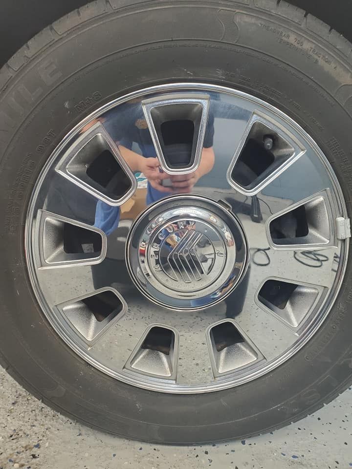 Close-up of a chrome truck wheel with black tire and reflective hubcap showing a person’s reflection