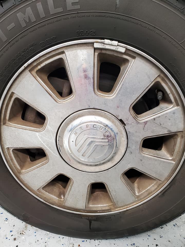 Close-up of a silver car wheel with a worn tire and hubcap bearing a logo.