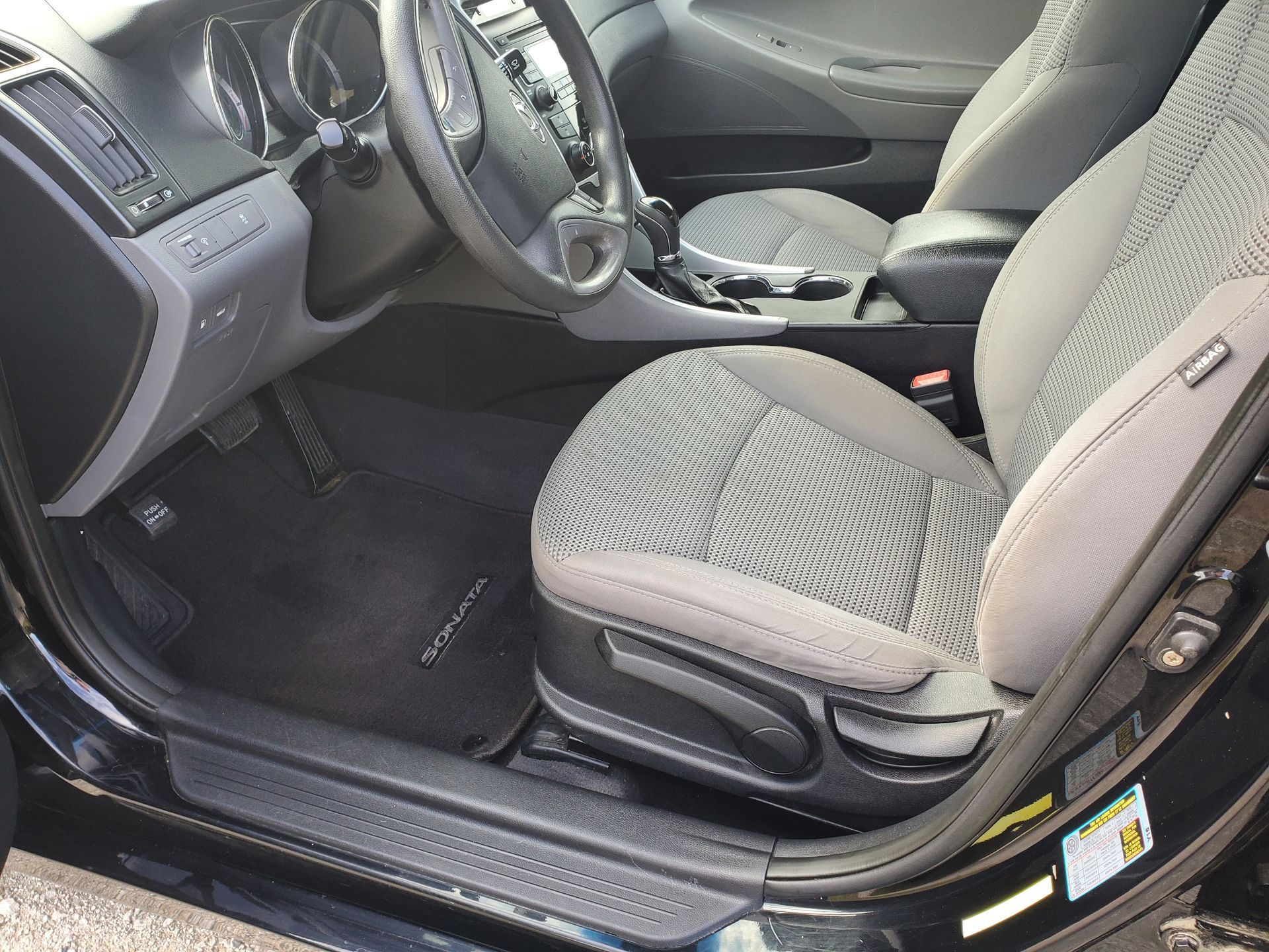 Front interior of a car with gray seats and black floor mats, passenger door open.