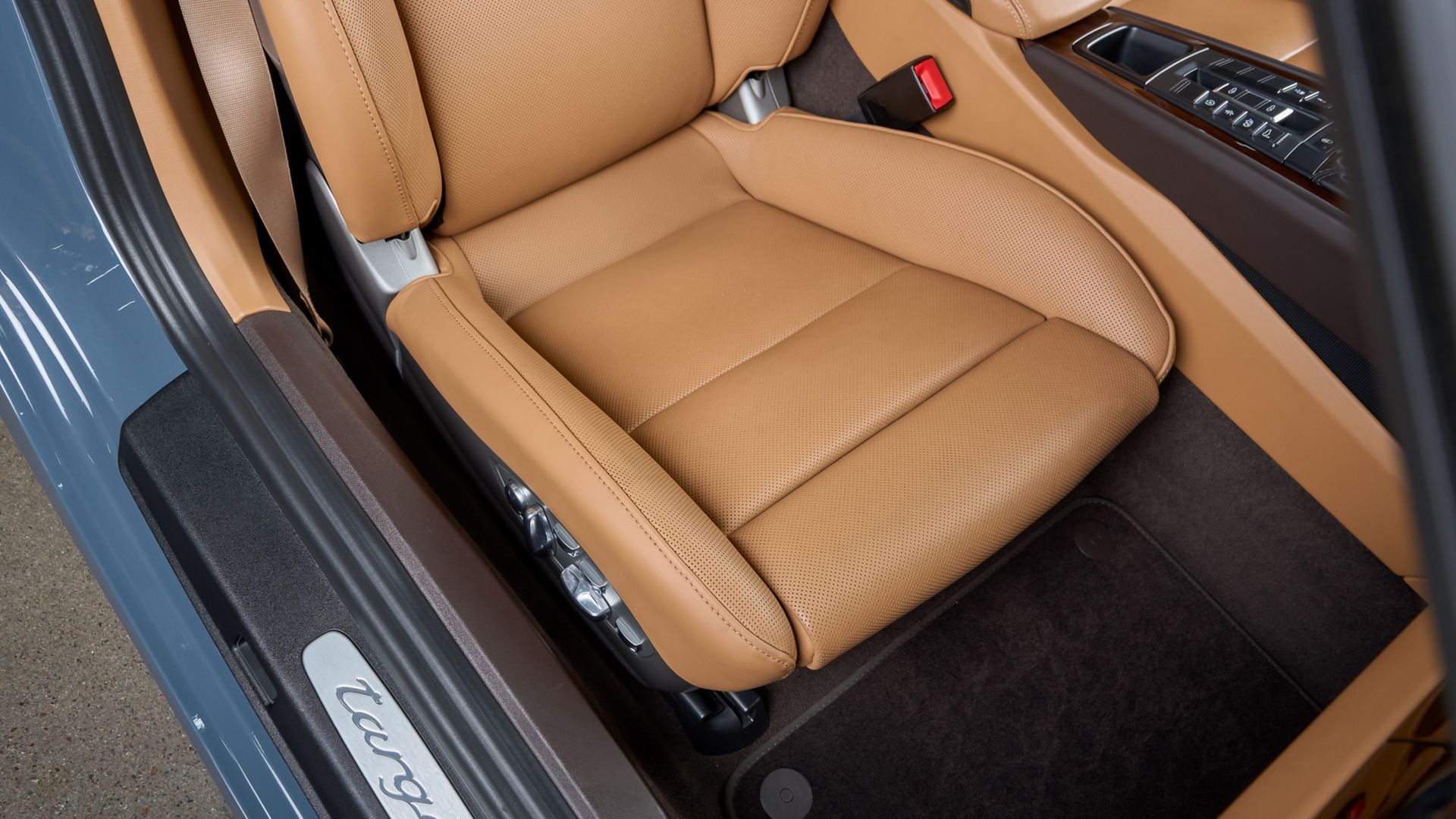 Tan leather car seat beside an open door, with black floor mat and silver door sill trim.