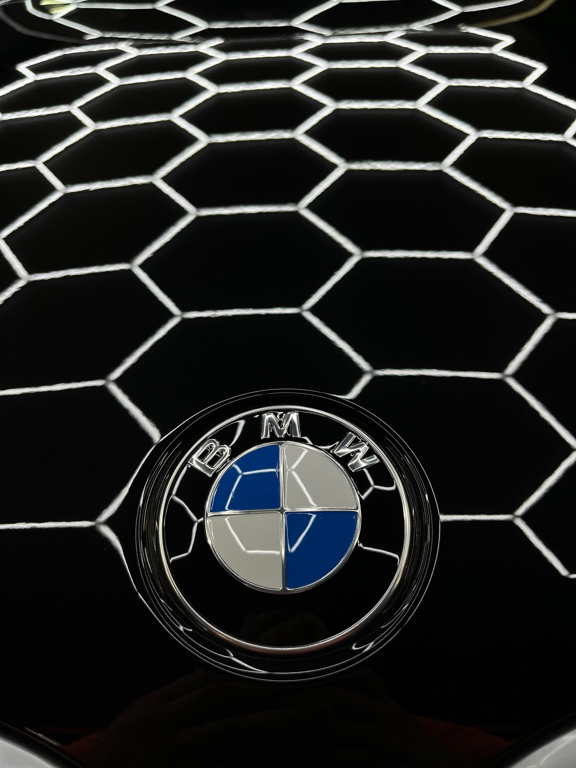BMW logo on a glossy black hood with a white hexagon pattern reflection