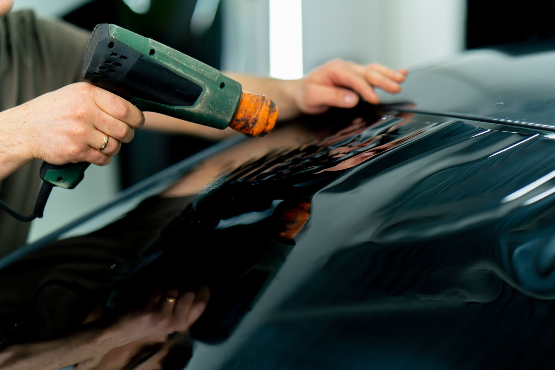 Person using a heat gun to remove vinyl wrap from a car hood