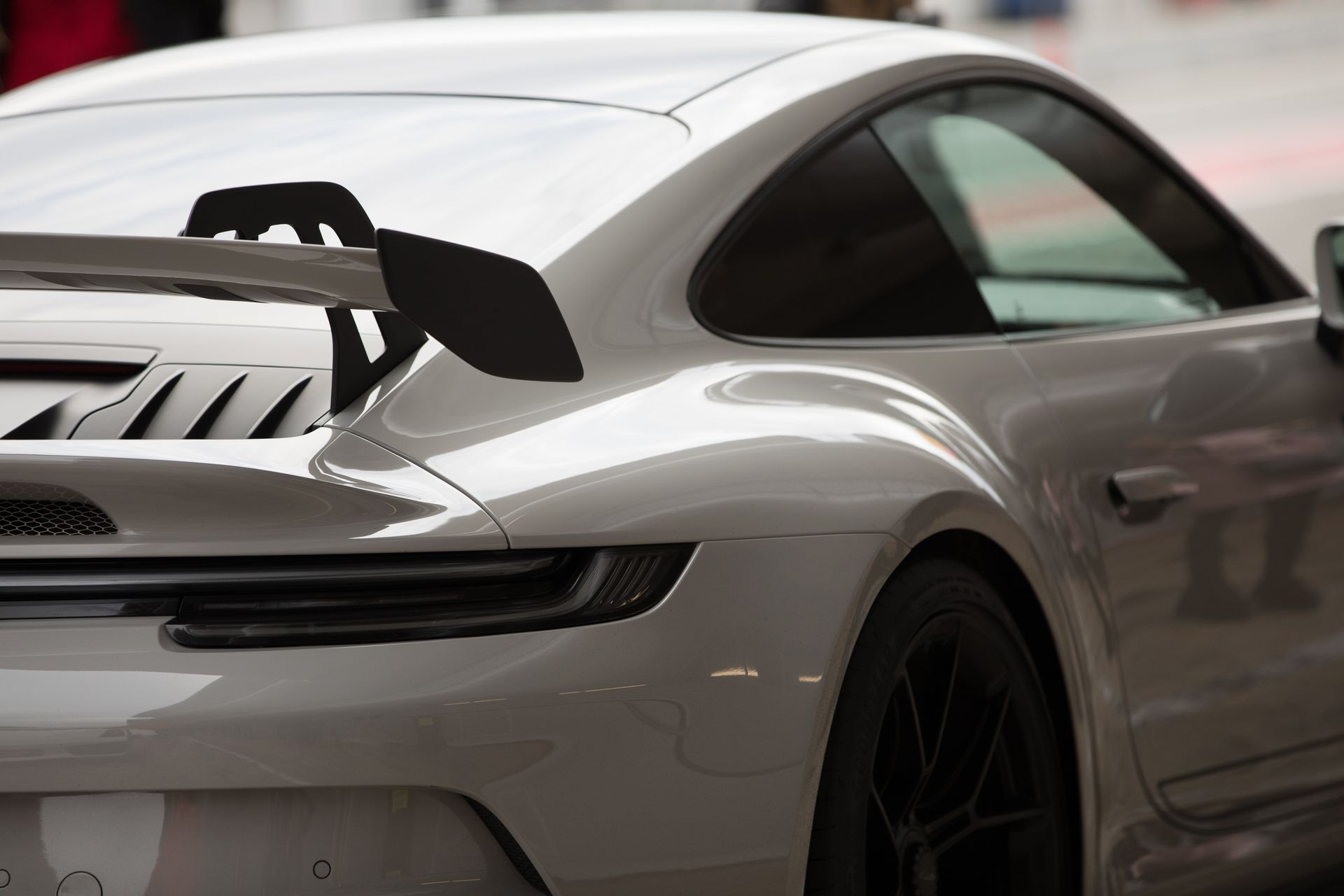White sports car with large rear spoiler, seen from the side in a garage or showroom.