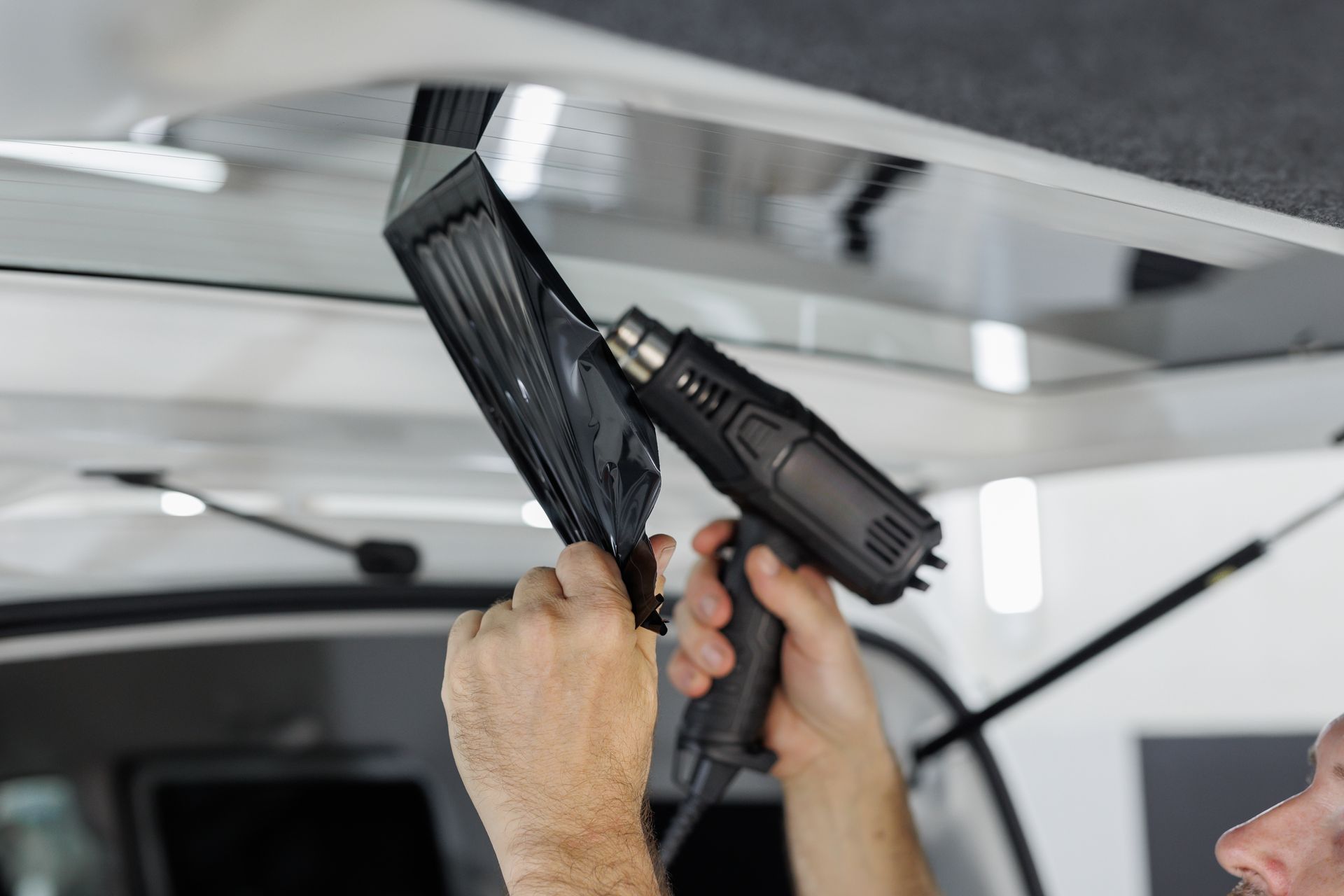 Hands using a drill to remove or install a ceiling panel inside a vehicle.