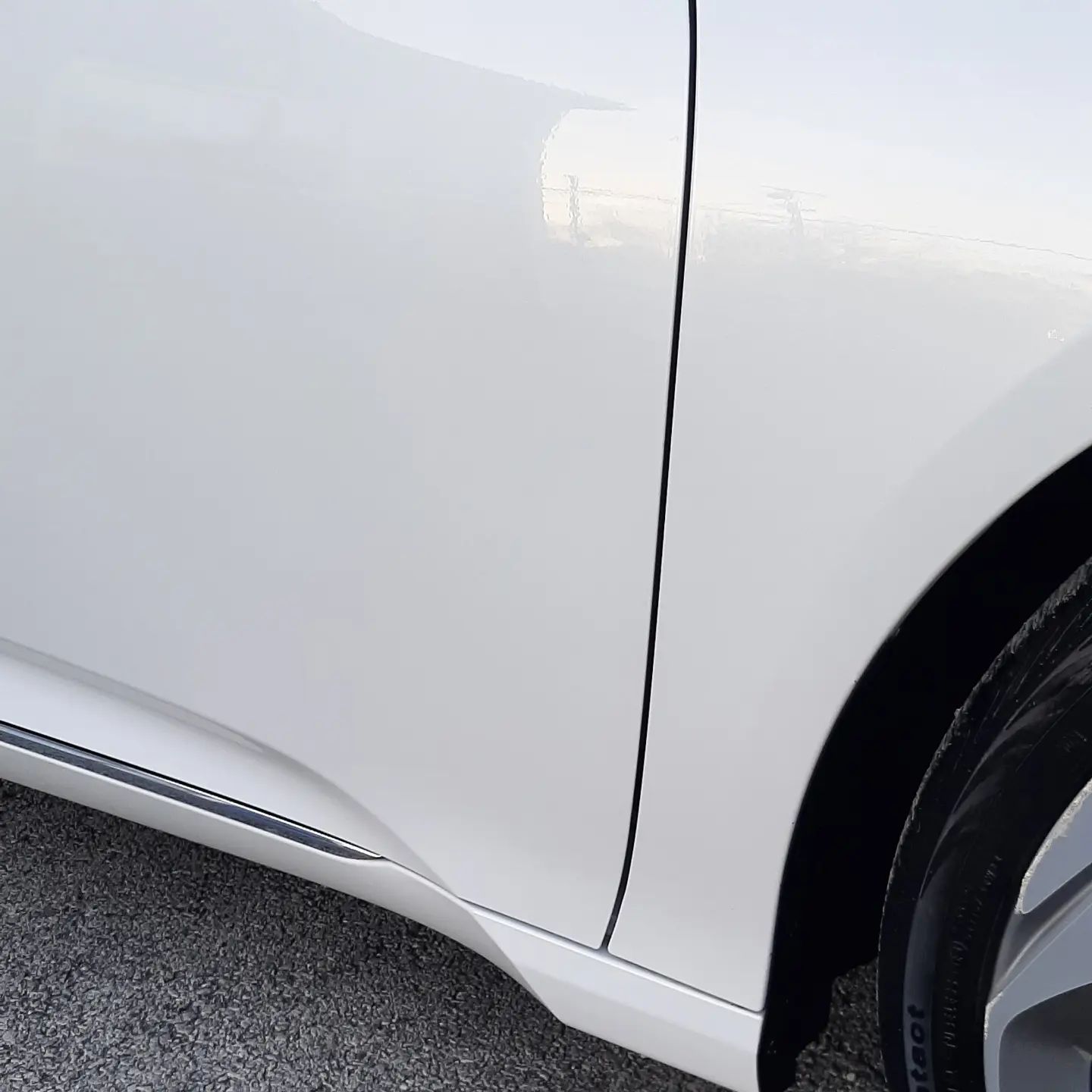 Close-up of a white car’s side panel, door seam, and wheel arch.