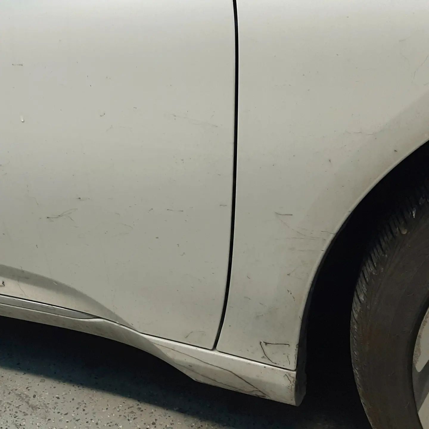 Close-up of a white car door and front wheel arch with a small dent and scuff mark.