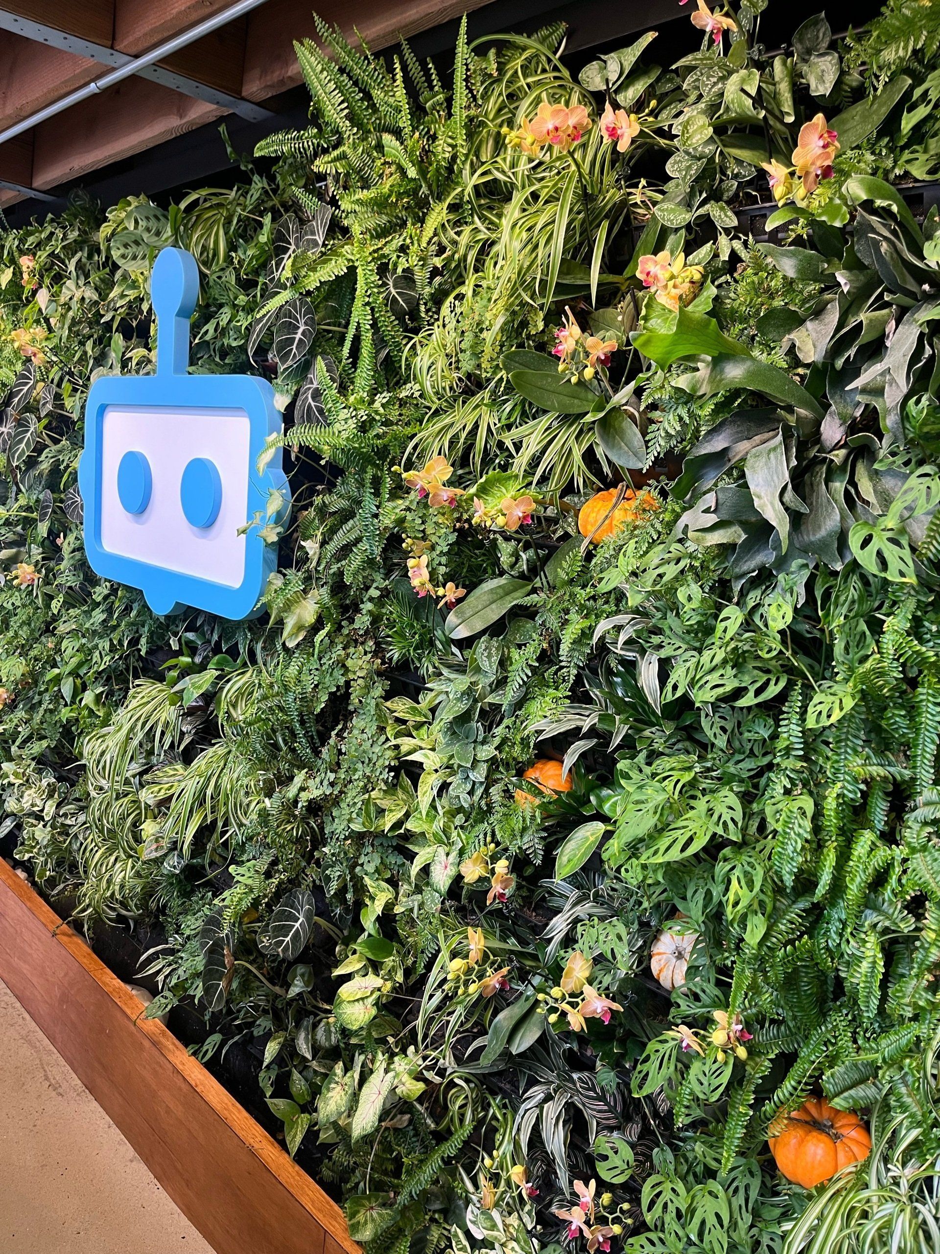 A wall of plants with a blue robot logo on it.