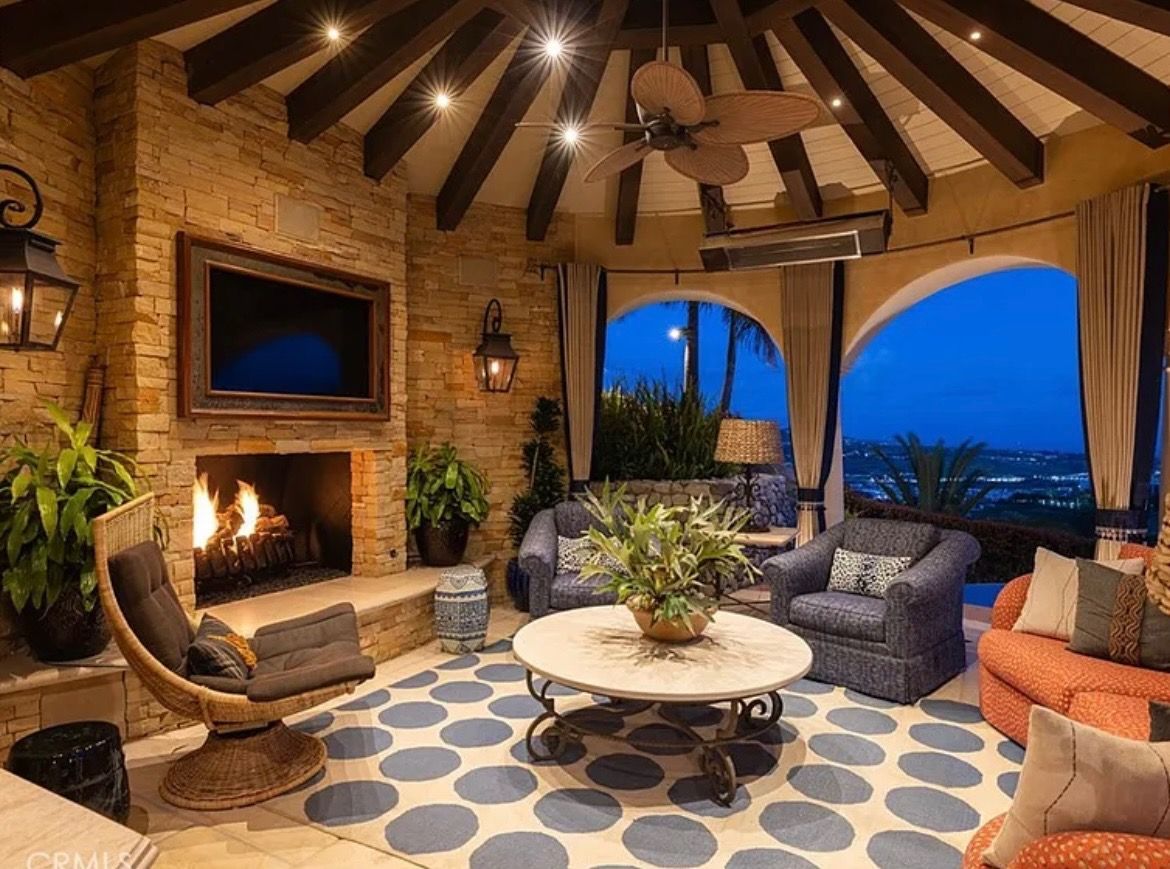 Cozy covered patio with fireplace, blue patterned rug, wicker chairs, and ocean view at dusk