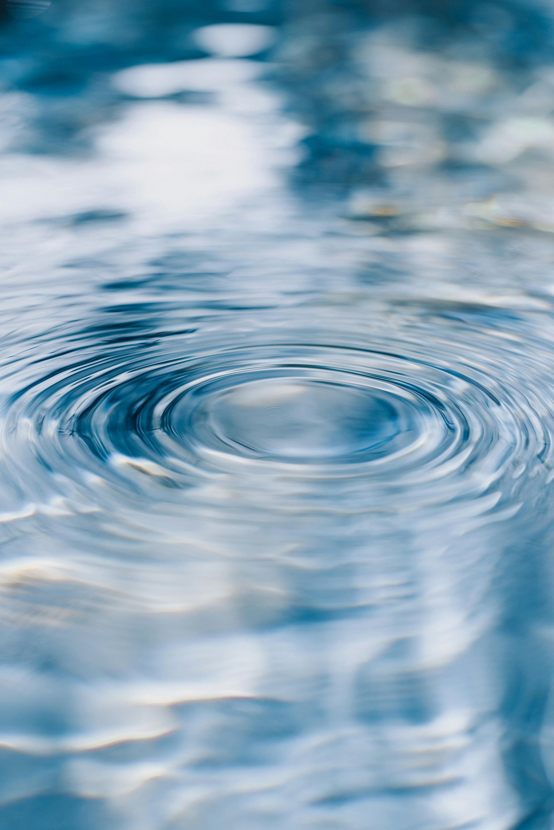 Concentrical ripples expand outward on the calm, light blue surface of water.