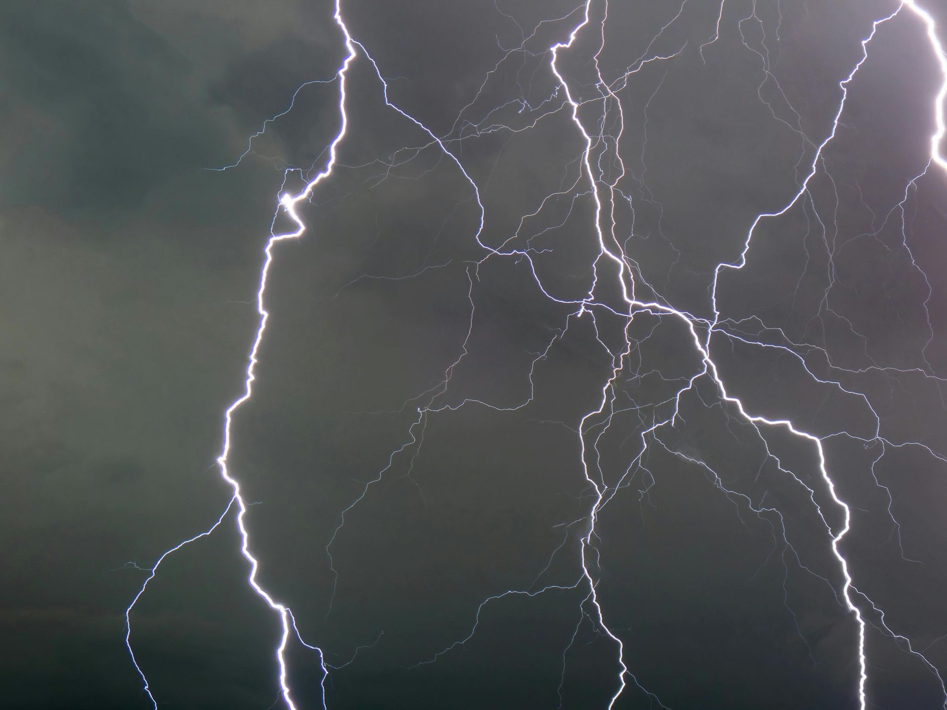 Bright, jagged lightning bolts strike across a dark, stormy, purple-tinted sky.