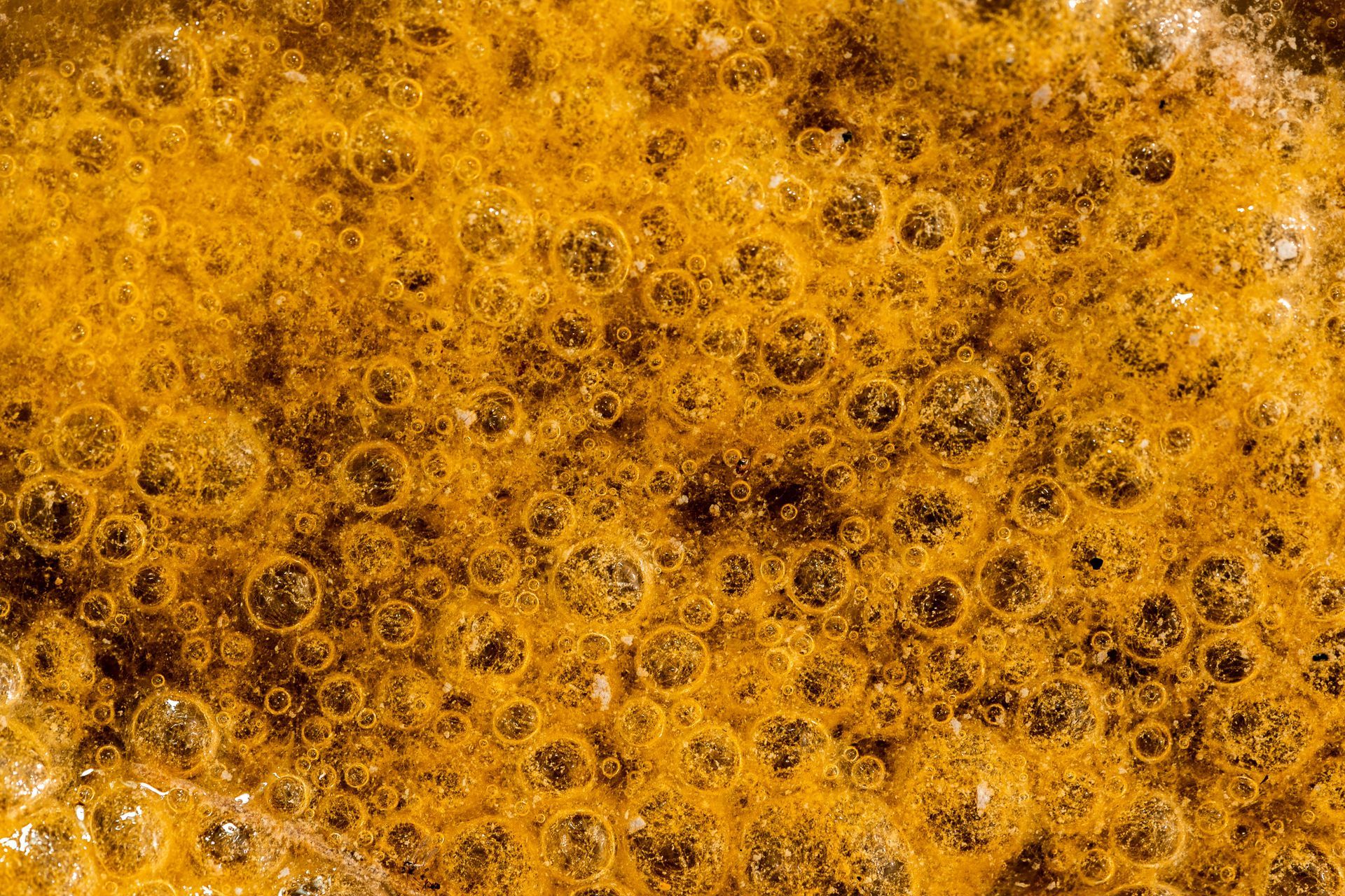 Close-up of bubbling, golden-brown caramel cooking in a pan, featuring many circular bubbles.