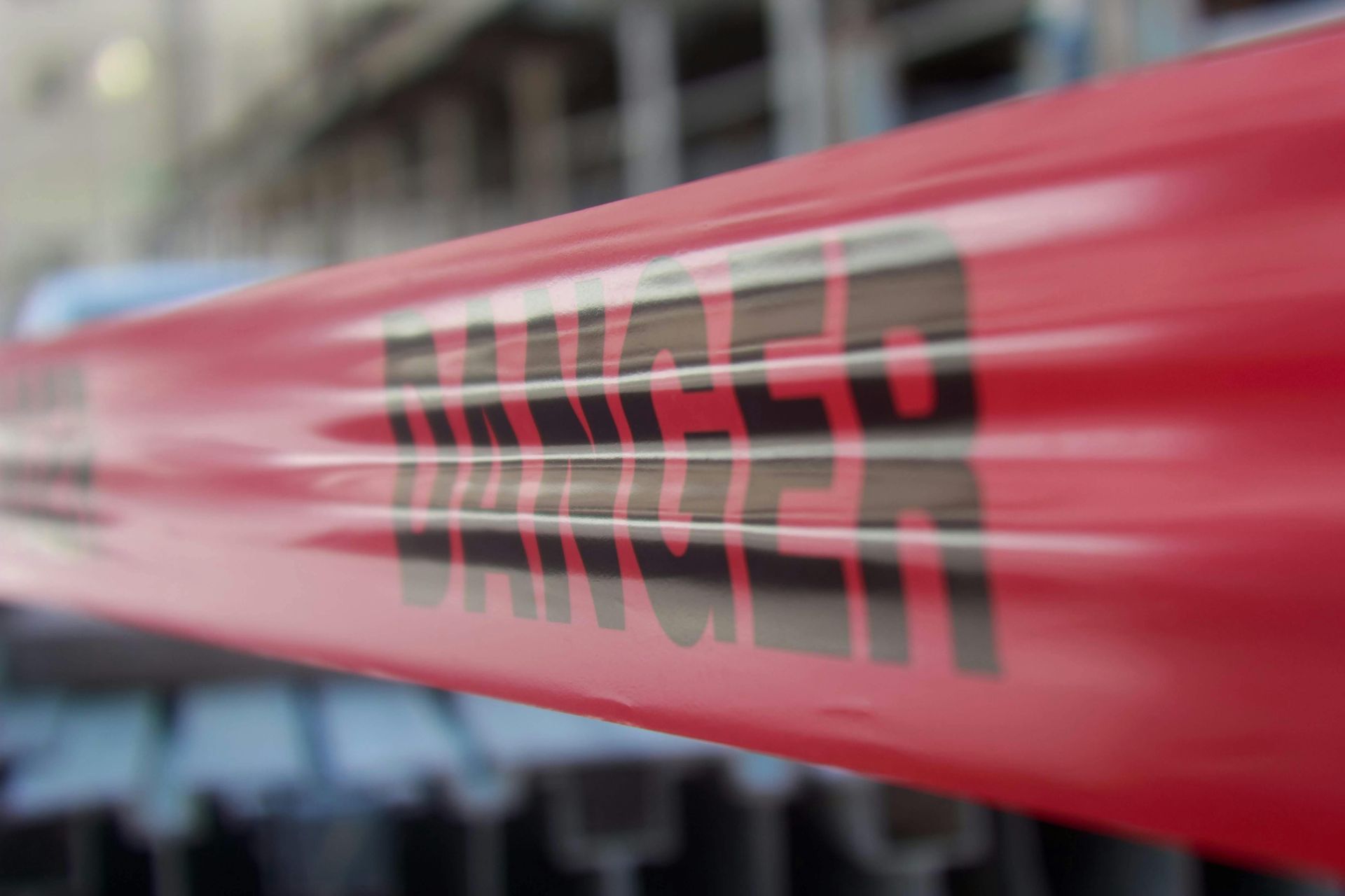 A close-up of bright red caution tape with the word DANGER printed in black bold letters, slightly out of focus.