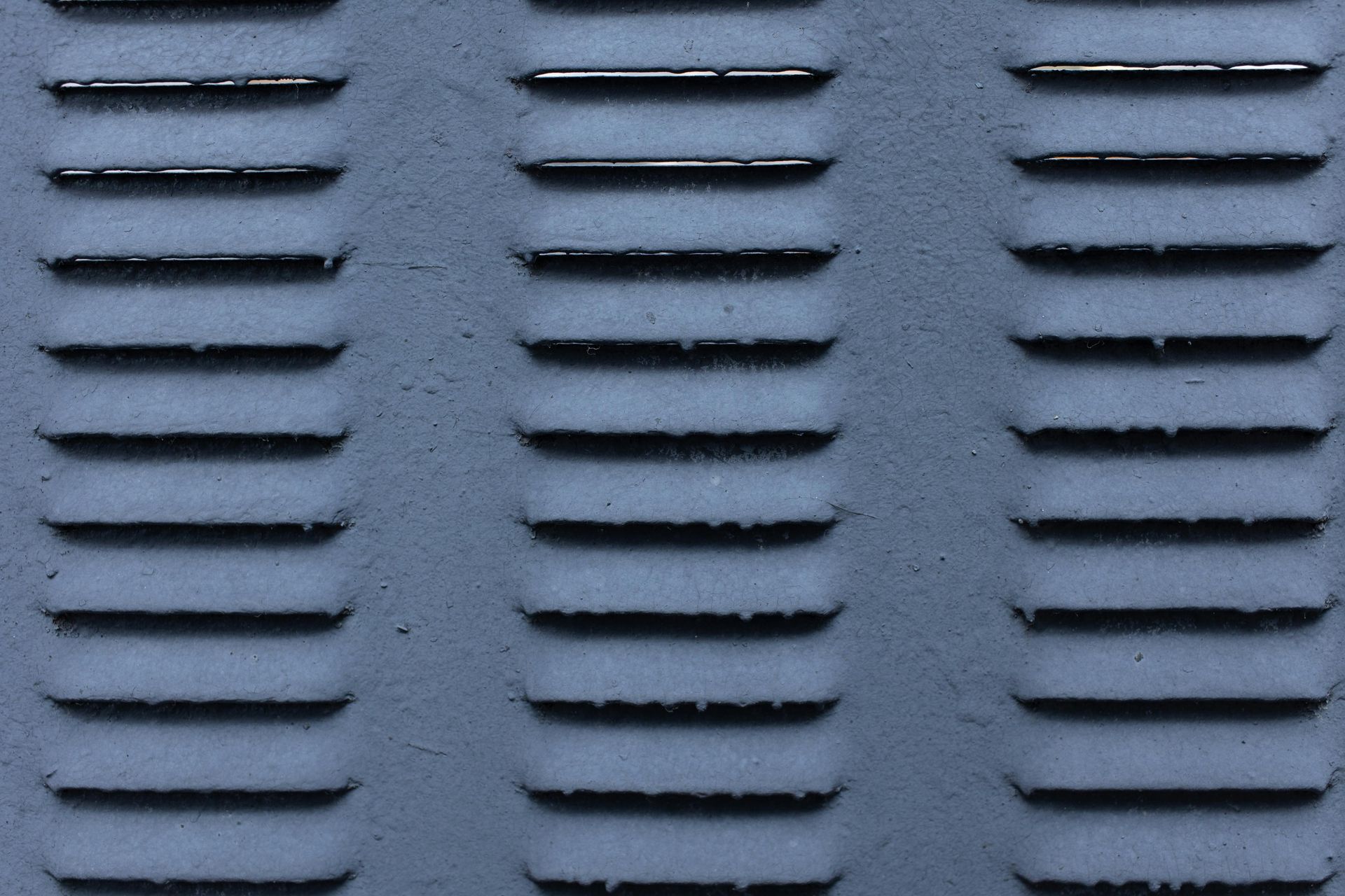 A textured gray metal surface with three columns of horizontal ventilation louvers.