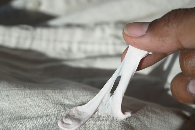 A person pulls a sticky, white substance, possibly chewing gum, off of a light-colored, wrinkled fabric.