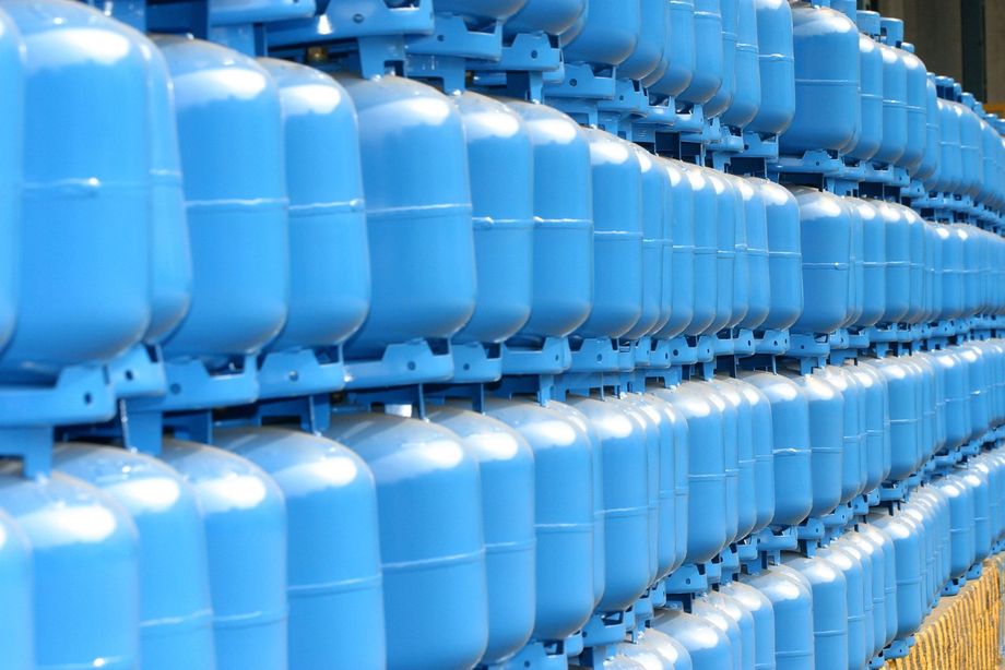Filas de cilindros de gas azules apilados en un área de almacenamiento similar a un almacén.