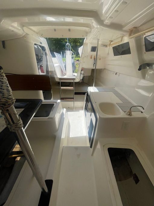 White yacht cabin with benches, a sink, and an open doorway to the deck.