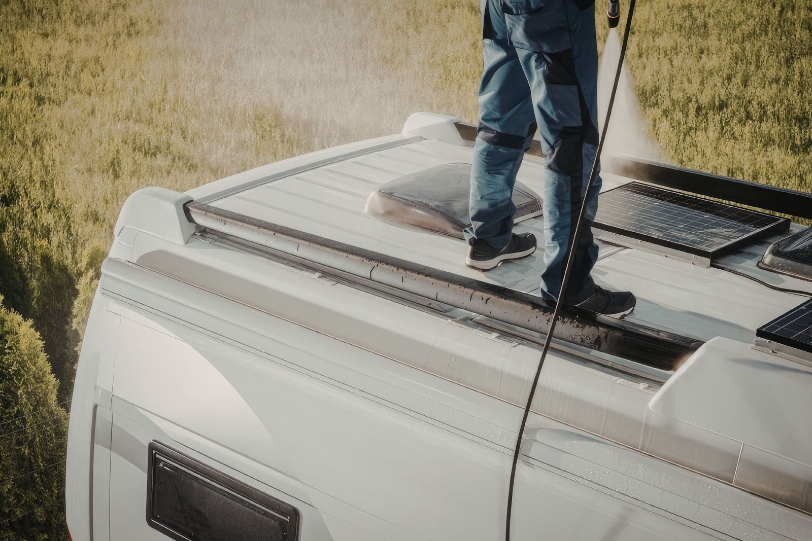 Person standing on the roof of a white van with cleaning tools on a grassy slope