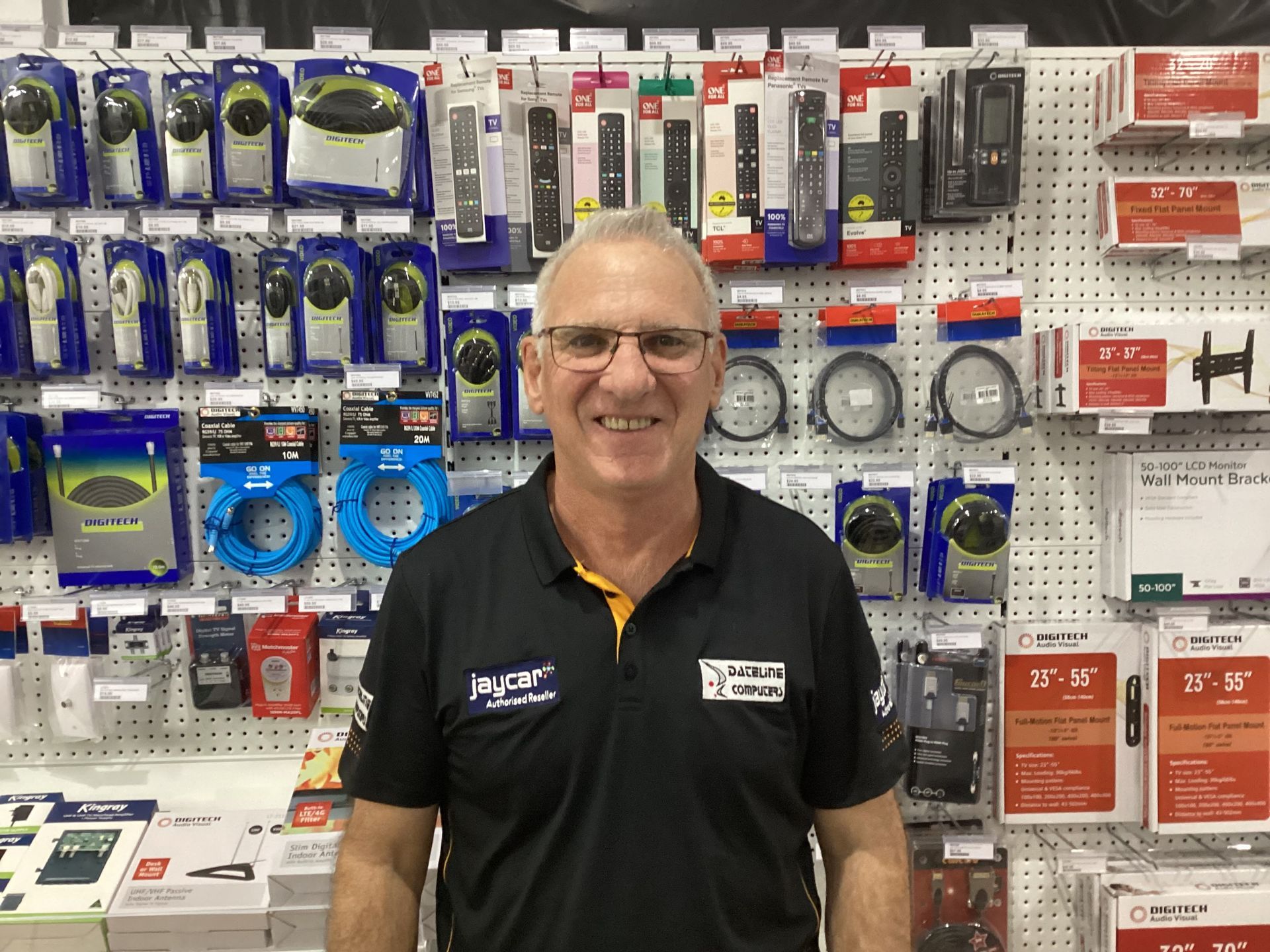 Smiling man in black polo stands in a hardware store aisle with electrical products on display