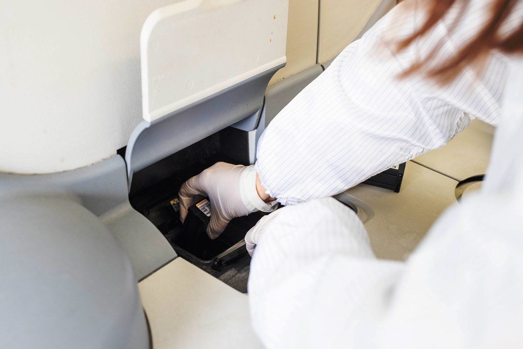 Persona in camice e guanti che inserisce qualcosa in una macchina, probabilmente per un esperimento scientifico.