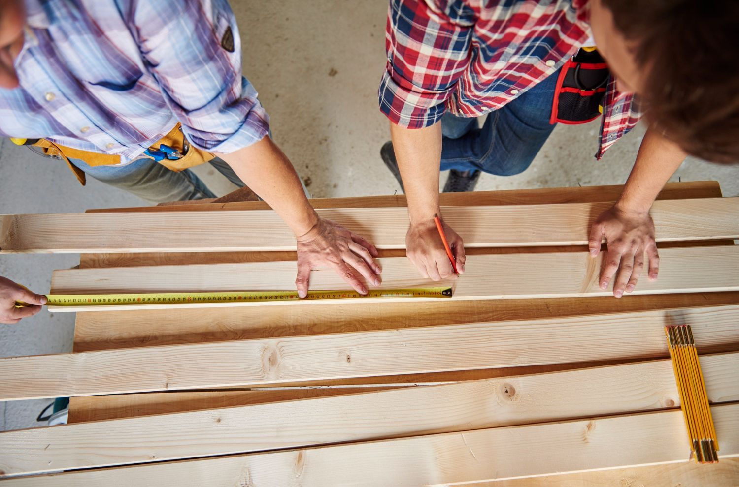 Two people are measuring a piece of wood with a tape measure.