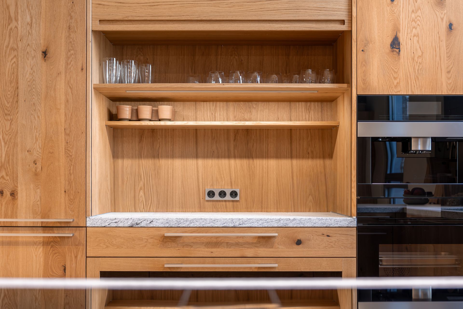 Modern kitchen with wood cabinets, open shelves, and a built-in black oven