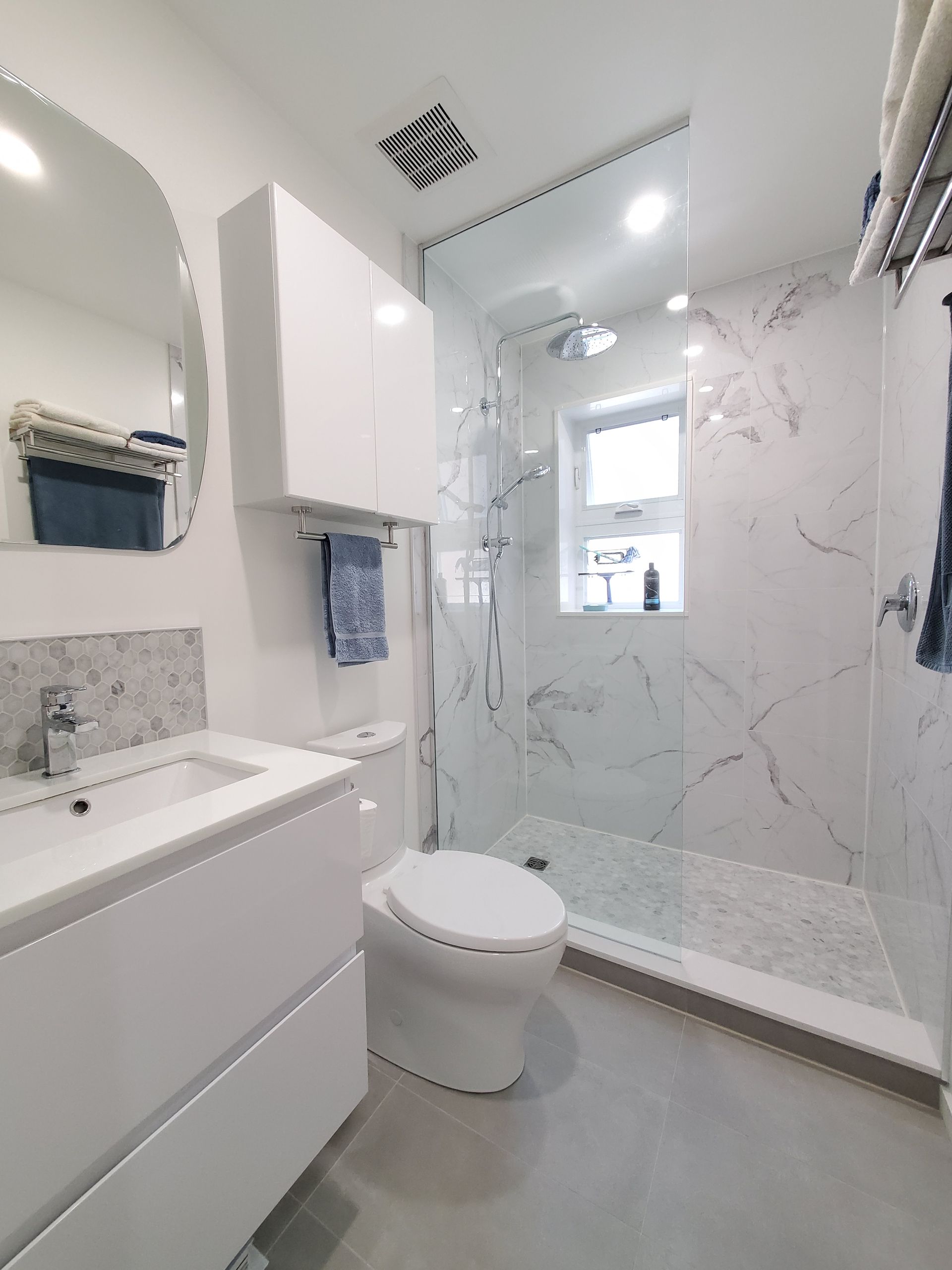 A bathroom with a toilet , sink , mirror and walk in shower.