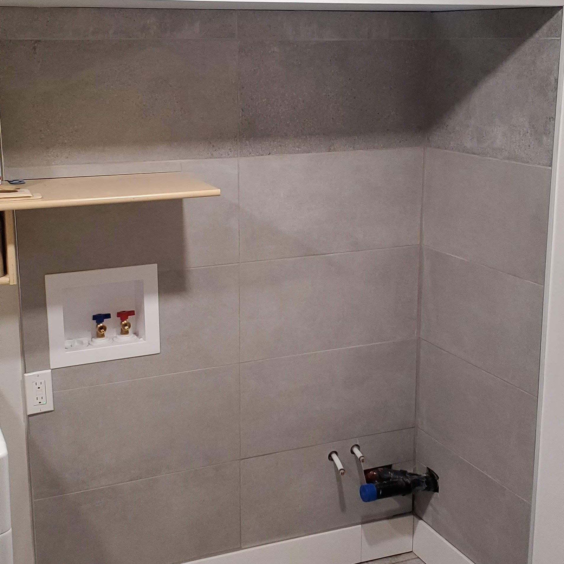 A bathroom with a shelf and a washer and dryer and tiles