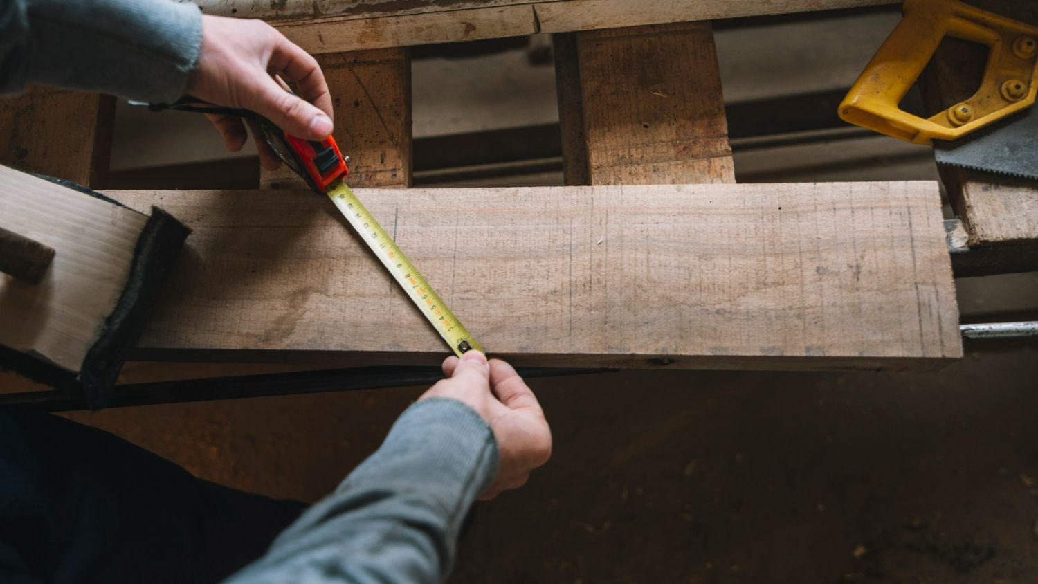 A person is measuring a piece of wood with a tape measure.