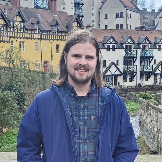 Person smiling outdoors with historic European-style buildings in the background